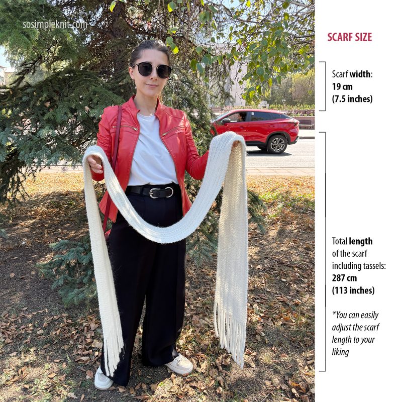 A woman stands outdoors, holding a long, cream-colored reversible scarf with tassels. She wears a red leather jacket, black high-waisted pants, and sunglasses. The background features green trees and a blurred car on the street. The scarf is draped in front of her, showing its length and texture. Text on the right side provides scarf size details, including width and total length, with a note about adjusting the length.