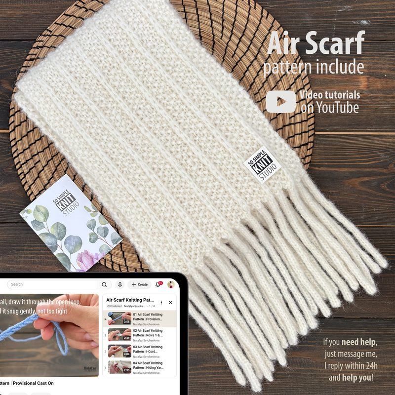 The image features a long, reversible knitted scarf displayed on a round woven mat. The scarf is light cream in color with a textured stitch pattern and has long, knotted fringes at one end. In the foreground, a tablet shows a partial view of a knitting video tutorial alongside two small cards, one of which includes the phrase "Air Scarf Knitting Pattern." The overall composition is warm and inviting, with natural textures and a cozy, hand-crafted feel.