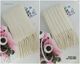 The image features a long, reversible cream-colored scarf displayed flat, with one side showcasing a textured stitch pattern and the other side featuring a ribbed design. The scarf has fringe at the ends and is accompanied by a small card with floral designs. The background is neutral, with soft pink accents from surrounding decorative elements. The scarf is neatly arranged, emphasizing its dual style.