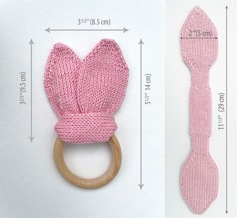 The image features a knitted bunny ears teething ring, displaying two textured pink ears and a wooden circular ring. The ears are positioned upright, showcasing a ribbed pattern, while the base of the ears has a knitted band connecting to the ring. The background is neutral, allowing the pink and wooden colors to stand out. Dimensions of the teething ring and the individual ears are indicated in simple labels next to the images, providing size context. The overall composition is clean and focuse