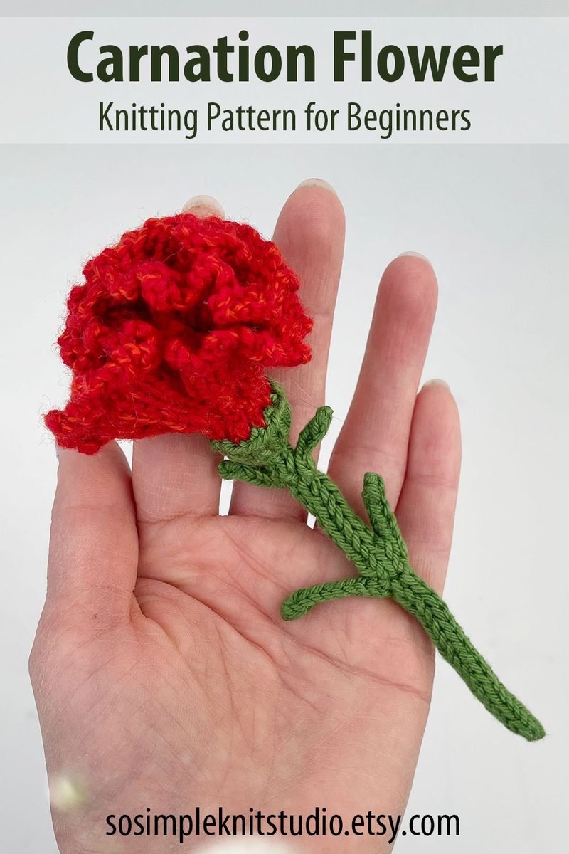 A hand holds a handmade carnation flower in vibrant red yarn, featuring layered petals and a green knitted stem with leaves, set against a plain white background. The top of the image includes the title "Carnation Flower" and the text "Knitting Pattern for Beginners" in a simple, modern font.