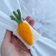A woman is holding a knitted carrot napkin ring in her hands against a white background. This is a knitting pattern for needle knitting.