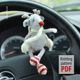 A knitted reindeer toy hangs from the steering wheel of a car. The reindeer is gray with a round body, white antlers, and a red nose. It has red and white striped legs and arms. The background shows a blurred dashboard with circular gauges, and a white square with the text "Knitting pattern PDF" in red. The overall scene is bright and focused on the reindeer, drawing attention to its playful design.