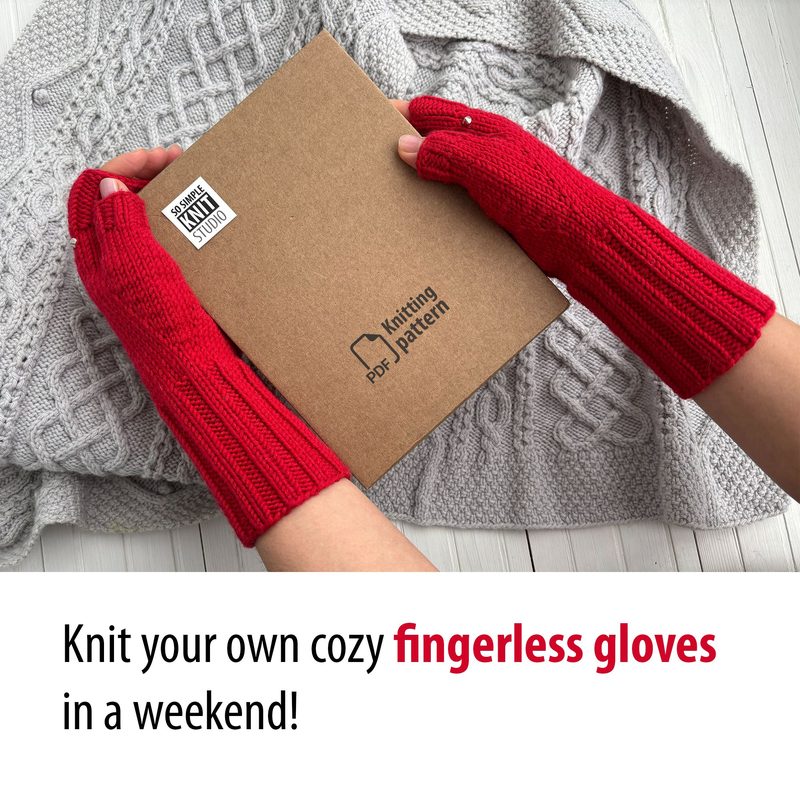 A pair of knitted red fingerless gloves are worn on hands that are holding a brown knitting pattern booklet. The background features a light gray, textured knitted fabric. The gloves have a ribbed design, and the overall composition is centered with the gloves in focus, creating a cozy atmosphere.