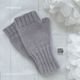 The image features a pair of light gray fingerless gloves knitted in a ribbed pattern, displayed on a textured white surface. The gloves have a snug fit with a ribbed cuff at the wrist. In the background, soft white paper flowers are partially visible, adding a delicate touch to the composition. A small logo tag reading "SO SIMPLE KNIT STUDIO" is placed between the gloves and the bottom edge of the image.