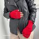 The image features a pair of red fingerless gloves worn by a person whose hands are positioned near their body. The gloves have a ribbed texture and are adorned with small silver studs along the edges. The individual is wearing a black leather jacket, partially unzipped, and beige pants. The background appears light-colored, and the overall lighting is bright, highlighting the gloves and jacket.
