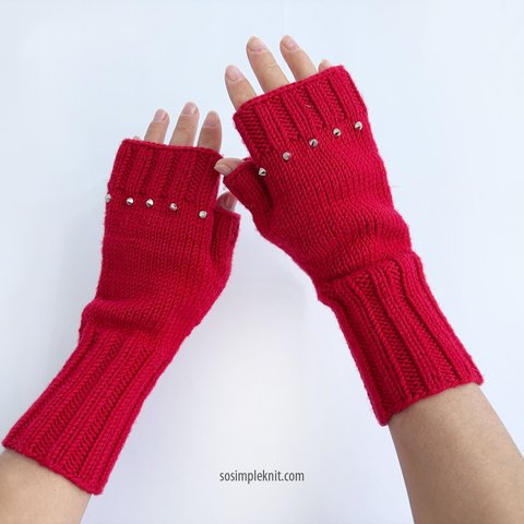 Red fingerless gloves with studs, worn on a woman’s hands, displayed on a white background, showing texture and design details.