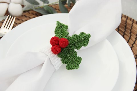 A knitted napkin ring in the shape of a Christmas holly leaf, with green leaves and red berries
