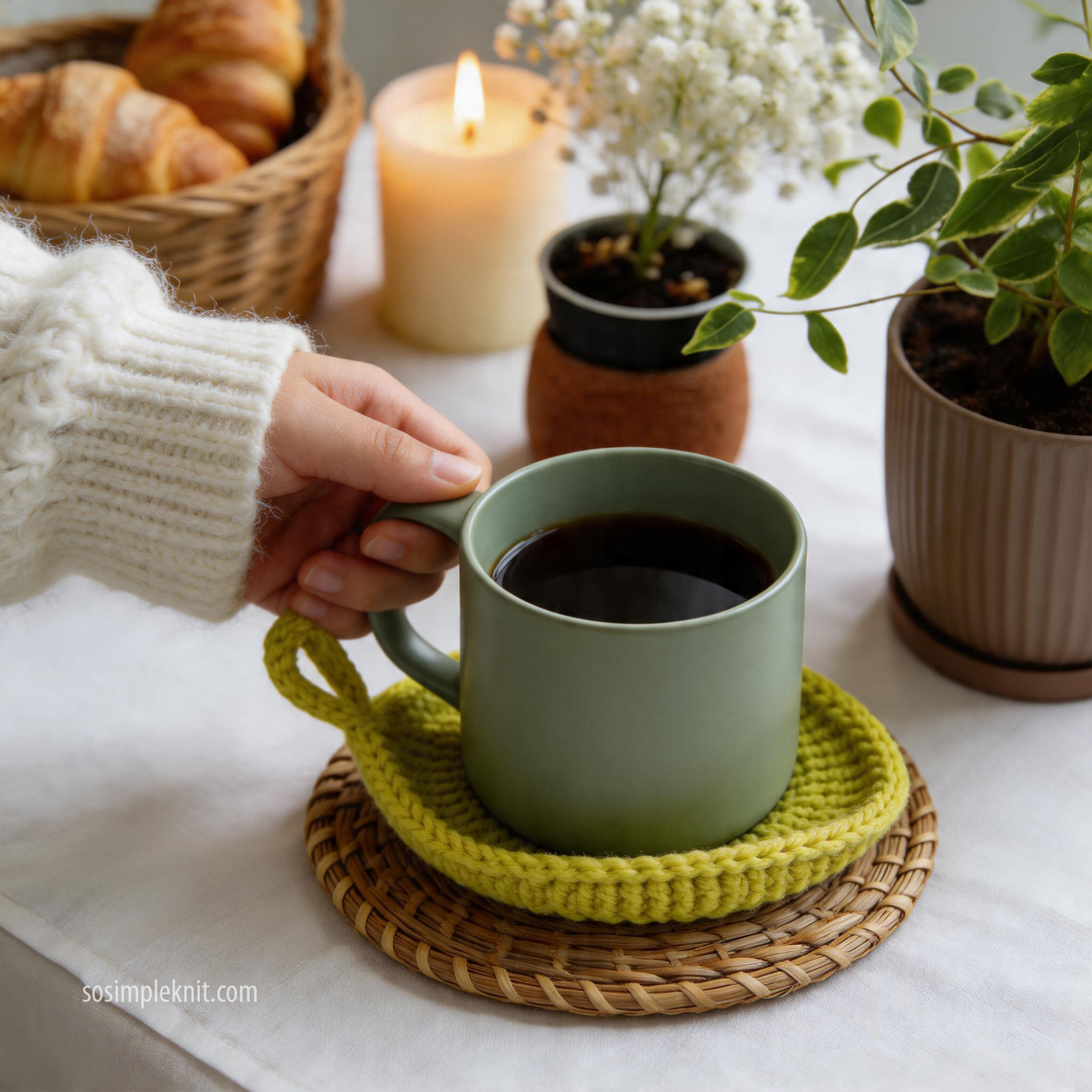 Lifestyle interior photo with a cozy atmosphere: a woman in a home setting holds a cup while another cup sits on a knitted leaf-shaped coaster on the table, showing everyday use of the Leaf Coaster.