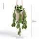 The image features a knitted pothos plant suspended in a beige crochet basket. The plant is adorned with multiple green, leaf-shaped pieces that hang down, mimicking the appearance of real pothos foliage. The colors used are various shades of green for the leaves and a light tan for the basket. A ruler on the side indicates the height of the plant arrangement, which is approximately 37 cm (14.6 inches) tall and about 14 cm (5.5 inches) wide. The background is plain and unobtrusive.