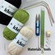 The image features three skeins of yarn in black, green, and cream, labeled "ideal" by YarnArt, arranged at the bottom. Above the yarn, there are knitting needles in various sizes, including green plastic and metal options, along with a pair of scissors, a tape measure, and several stitch markers. The elements are neatly organized against a white background, with the text "Materials & tools" prominently displayed in bold black font.