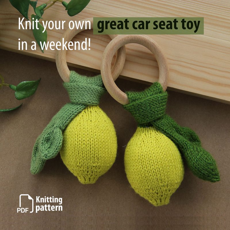 The image features two knitted lemon toys attached to wooden rings, one lemon has a green leaf and a green scarf, while the other is similar in design. The lemons are bright yellow with a textured knit pattern. The background includes light brown wood and green foliage, creating a natural and cozy setting. Text on the image states "Knit your own great car seat toy in a weekend!" and includes a graphic of a PDF symbol and the words "Knitting pattern." The overall color scheme is cheerful, with ye