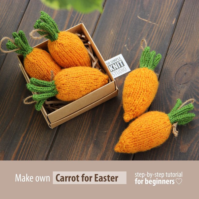 The image features a small box containing several knitted mini carrots. The carrots are bright orange with textured knitting and have green knitted tops that resemble leaves. There are also a few loose mini carrots placed beside the box. The background is a neutral wood surface, and the overall composition is simple and focused, highlighting the knitted items. The text at the bottom promotes a DIY tutorial for making the carrots.