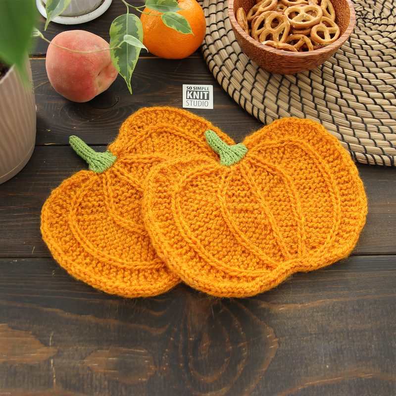 Two knitted orange pumpkins with green stems. Knitting pattern for a pumpkin-shaped mug coaster