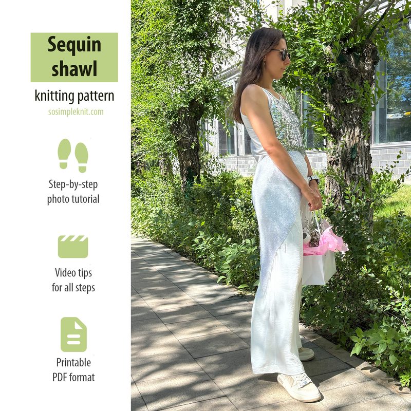 A woman stands outdoors wearing a fitted, sleeveless top and a long, sequined shawl, which glimmers in the sunlight. She is facing sideways, with a white handbag in one hand and pink items peeking out. The background features green foliage and a modern building, with sunlight casting soft shadows. The overall color scheme includes silver sequins, white clothing, and green greenery. The composition is framed to focus on the woman and her shawl, with a blurred background.
