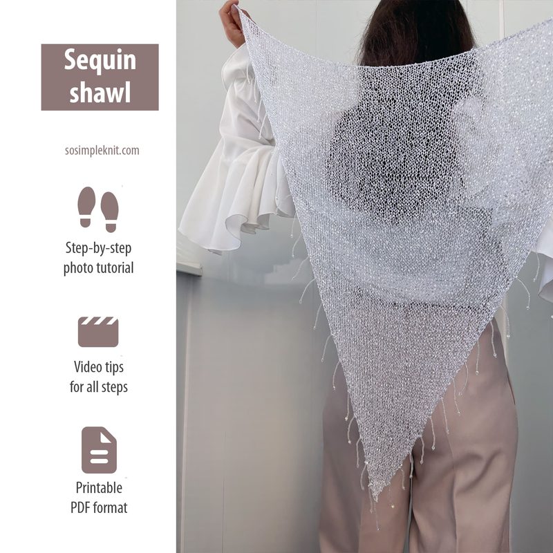 A person stands with their back to the camera, holding a semi-transparent triangular sequin shawl made of shimmering silver yarn. The shawl drapes down and has fringed edges, reflecting light. The wearer is dressed in a white blouse with ruffled sleeves and light-colored trousers. The background is a plain wall, enhancing the focus on the shawl. Text on the side indicates it's a sequin shawl pattern with details about a tutorial and PDF format.