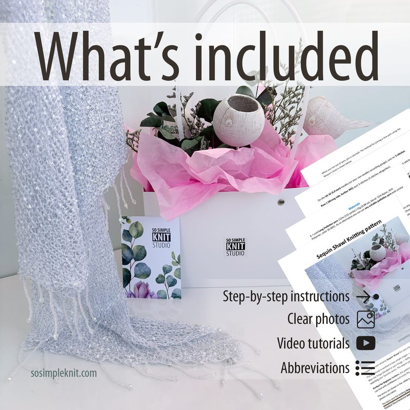 A light gray sequin shawl drapes elegantly alongside a white gift bag with pink tissue paper, surrounded by greenery and decorative items. The shawl features delicate fringe at the ends, showcasing textures that shimmer in the light. Near the bag, there are printed sheets displaying the "Sequin Shawl Knitting Pattern" and additional materials like a business card and an informational flyer, all arranged on a clean, bright surface.