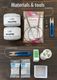 The image shows a flat lay of knitting materials and tools arranged on a dark wood surface. There are two skeins of yarn labeled "LANG PAILLETTES" in a light silver color. A set of knitting needles is enclosed in a plastic package, accompanied by a charm and small scissors. To the right, there is a small spool of thread and various packets of beads labeled "PRECIOSA." A cardboard box is placed in the bottom right corner.