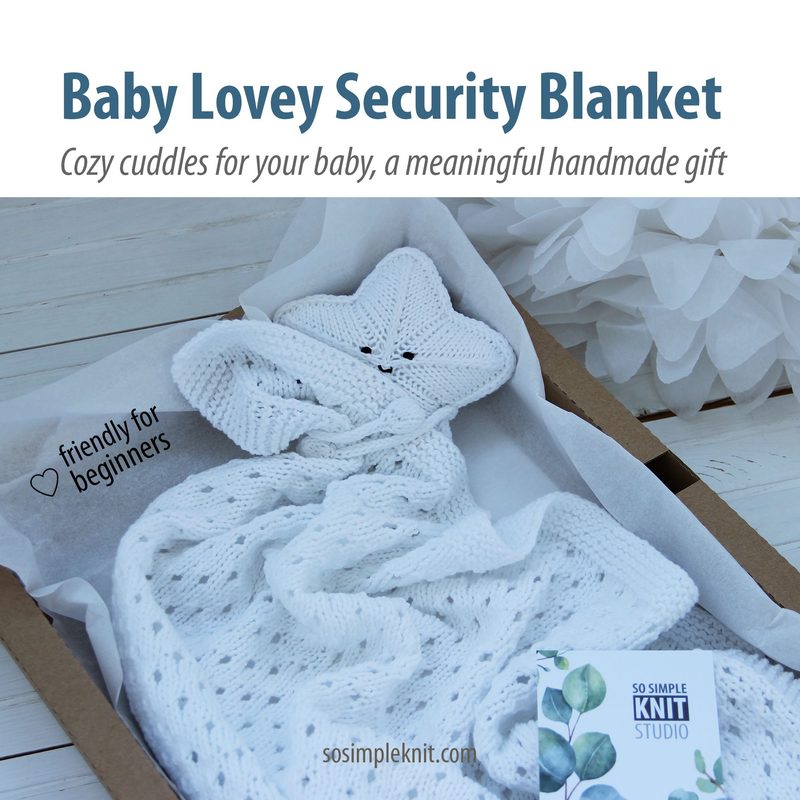 The image shows a soft, knitted baby lovey security blanket with a star-shaped head and arms made of white yarn. The blanket features textured patterns and a gentle drape, with the head appearing at the center. It is arranged in a light-colored box lined with a soft, neutral fabric. In the foreground, a small card displays the brand name "SO SIMPLE KNIT STUDIO." The overall color scheme is soft and calming, with pastel tones. The framing emphasizes the blanket as the central focus against a ligh