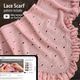 The image features a light pink lace triangle scarf displayed on a wooden surface, showcasing an intricate knitted pattern with small holes throughout. There is a decorative ruffled edge along one side of the scarf. In the bottom left corner, a digital device displays a knitting tutorial video related to the scarf pattern, with visible text instructing viewers on the technique. The overall composition is warm and inviting, emphasizing the texture of the knit fabric.